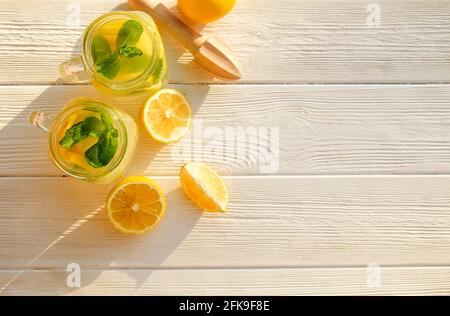 Deux verres de mason pot de limonade rafraîchissante maison avec des tranches de citron biologique mûr, entier et divisé en deux, centrifugeuse, mudler, presse-fruits sur un blanc rustique Banque D'Images