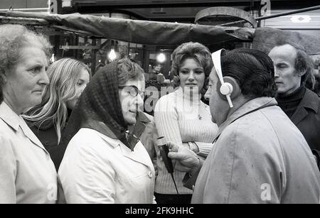 Années 1970, homme populaire du peuple, présentateur et journaliste à la radio, Monty Modlyn, enregistrant l'opinion d'une femme locale, avec d'autres personnes à l'écoute, à l'extérieur d'un marché du sud de Londres, Angleterre, Royaume-Uni. Né dans une famille juive de Lambeth, Modlyn était connu pour son accent de cockney et sa forte de diffusion interviewe les gens ordinaires, une technique qui est devenue connue sous le nom de 'Vox Pop'. S'adressant aux gens avec les mots « Ullo darlin », son personnage de classe ouvrière de l'est a vu qu'il avait des conversations sur tout et tout au cours d'une longue et distinguée carrière dans le domaine de la radiodiffusion. Banque D'Images