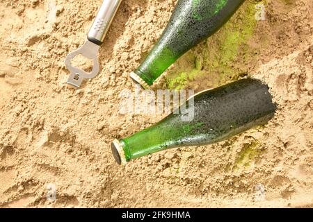 Détail des bouteilles de bière fraîche fermées sur le sable et un ouvre-bouteille sur le côté. Vue de dessus. Banque D'Images