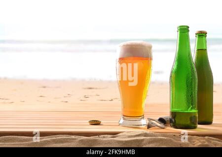 Verre de bière fraîche et deux bouteilles sur un bois dans le sable sur la plage avec la mer dedans l'arrière-plan Banque D'Images