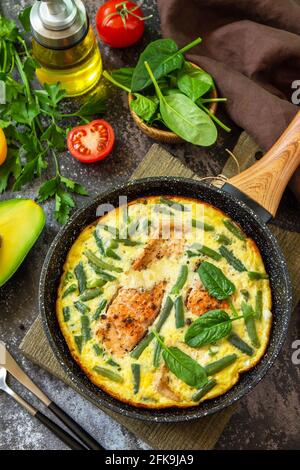 Petit déjeuner ou déjeuner en-cas. Omelette rustique (omelette, brouillée) avec filet de saumon et haricots verts dans une poêle sur fond de pierre. Banque D'Images