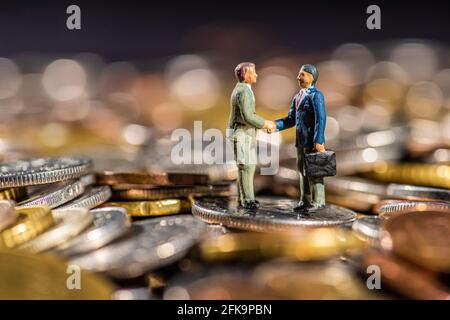 Petites figures de deux hommes qui se secouent la main sur un tas de pièces. Banque D'Images