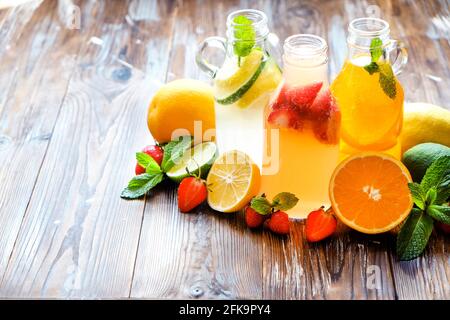 Trois bouteilles millésimes fraîches de limonade glacée, boissons aux goûts différents avec citron, orange, pamplemousse, citron vert, feuilles de menthe et fraise sur la courge grachée Banque D'Images