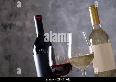 Deux bouteilles de vin rouge et blanc avec des étiquettes vierges noires et blanches mates sur fond de mur en béton. Verres à vin à moitié plein de vin ancien cher Banque D'Images