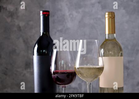 Deux bouteilles de vin rouge et blanc avec des étiquettes vierges noires et blanches mates sur fond de mur en béton. Verres à vin à moitié plein de vin ancien cher Banque D'Images