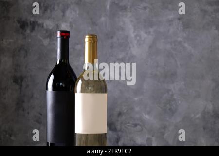 Deux bouteilles de vin rouge et blanc avec des étiquettes vierges noires et blanches mates sur fond de mur en béton. Des bouteilles de différentes couleurs vintage et chères. CLO Banque D'Images