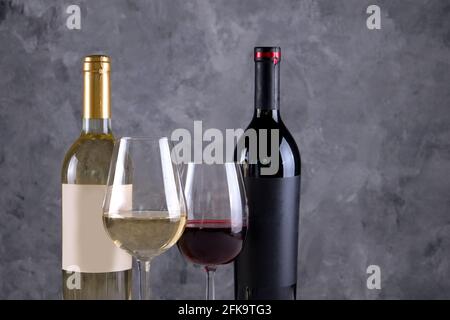 Deux bouteilles de vin rouge et blanc avec des étiquettes vierges noires et blanches mates sur fond de mur en béton. Verres à vin à moitié plein de vin ancien cher Banque D'Images