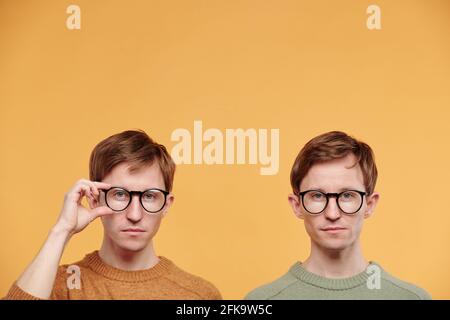 Portrait de vrais jumeaux intelligents dans des lunettes qui se posent contre arrière-plan orange Banque D'Images