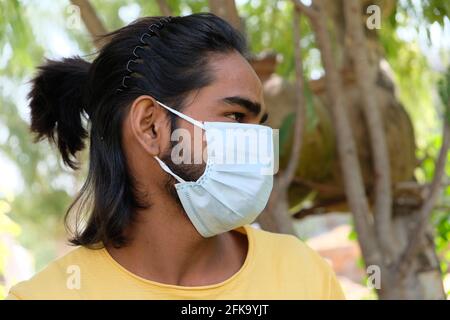 Portrait d'un jeune homme indien aux cheveux longs port d'un masque médical dans un parc Banque D'Images