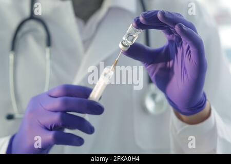 Médecin avec stéthoscope médical dans une robe médicale et protecteur les gants remplissent une seringue avec un vaccin Banque D'Images