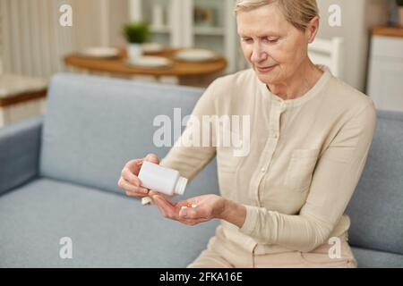 La femme âgée s'assoit sur le canapé ayant des vitamines ou des suppléments alimentaires quotidiens à la maison, la femme âgée mûre retraité prendre la dose de pilules de la bouteille de médicaments, personnes âgées Banque D'Images