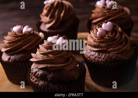 Délicieux cupcakes au chocolat noir, garniture en coeur de sucre, table texturée en bois. Boulangerie au cacao, café rustique en tranches d'arbre en bois, tabl de l'hippopotame Banque D'Images