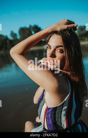 Portrait d'une femme brune confiante portant une robe rayée et poser près d'un lac dans un parc Banque D'Images