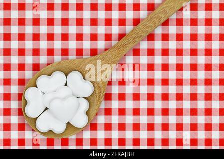 Une cuillère en bois pleine de pilules de bonbons en forme de coeur sur arrière-plan à carreaux vichy rouges Banque D'Images