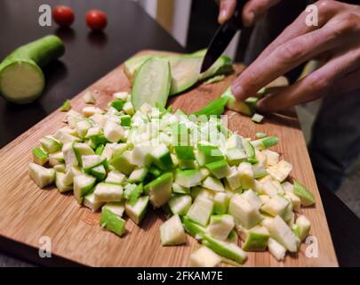 Fermez les mains du jeune homme coupé avec un couteau dans des tranches de concombre de courgettes sur une planche à découper en bois. Banque D'Images