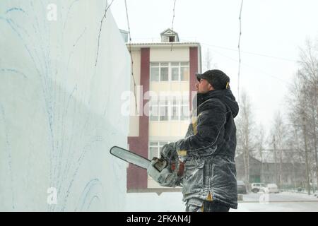 Le sculpteur coupe une figure hors de la glace par une tronçonneuse pour Noël Banque D'Images