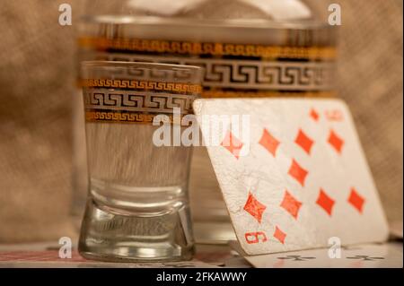 Jouer aux cartes, un verre de vodka et un carafe de vodka sur une table recouverte de gros burlap. Gros plan, mise au point sélective. Banque D'Images