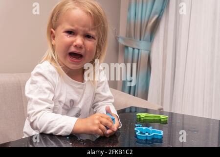 Pleurs caucasiens enfant joue avec la pâte de jeu colorée Banque D'Images