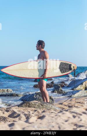 Surfer sur la plage holding est surf et regarder le vagues Banque D'Images