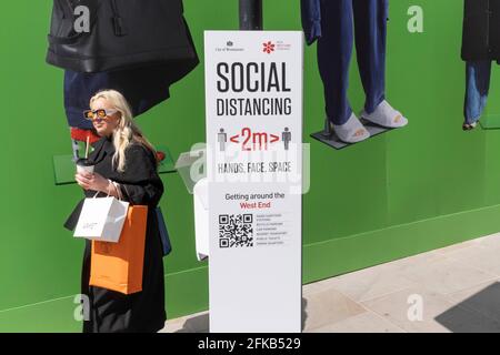 Une femme passe devant un signe de distanciation sociale Covid sous la palissade de construction temporaire pour Balenciaga, un espace de vente qui ouvrira bientôt sur Bond Street, le 27 avril 2021, à Londres, en Angleterre. Balenciaga est une maison de mode fondée en 1917 par le designer espagnol Cristóbal Balenciaga à San Sebastián, en Espagne. Banque D'Images