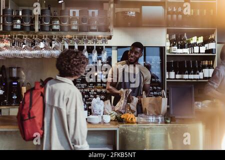 Une cliente qui parle avec un propriétaire masculin dans une épicerie fine Banque D'Images