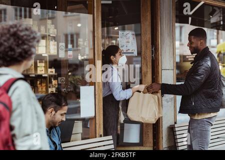 Un client de sexe masculin se charge de la collecte de la commande auprès d'un propriétaire de sexe féminin dans un magasin pendant une pandémie Banque D'Images