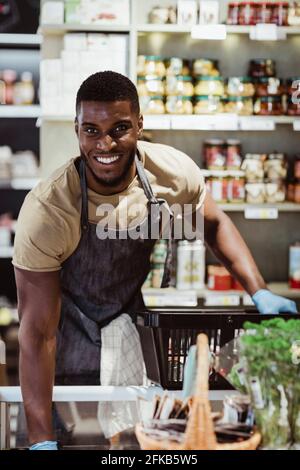 Portrait de propriétaire masculin souriant avec panier dans un magasin de charcuterie Banque D'Images