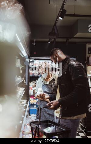 Un client de sexe masculin tient la nourriture dans son emballage tout en discutant avec une femme propriétaire en magasin Banque D'Images