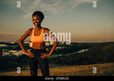 Athlète féminine souriante avec main sur la hanche au coucher du soleil Banque D'Images