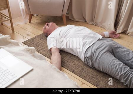 Homme caucasien méditant sur un plancher en bois et allongé dans la posture de Shavasana Banque D'Images