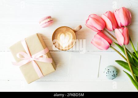 Gâteaux de désert de macaron français aux myrtilles et aux fraises, tasse de café de cappuccino brun, art latte en forme de coeur, papier artisanal enveloppé présent tulipe f Banque D'Images