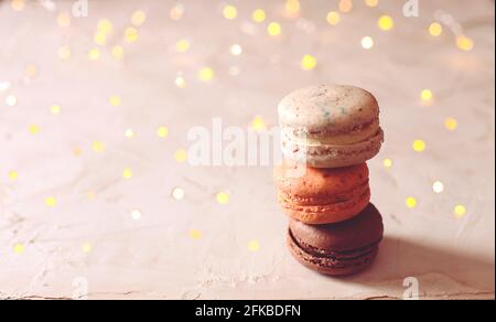 Composition élégante de macarons au chocolat aux amandes assorties français, lumières de noël sur une table texturée en plâtre de stuc blanc. Joyeux anniversaire mère wome Banque D'Images