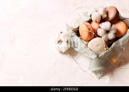 Composition élégante de macarons français dans une boîte, lumières en coton et de noël, table texturée en plâtre de stuc blanc. Joyeux anniversaire Valentin pour femmes Banque D'Images