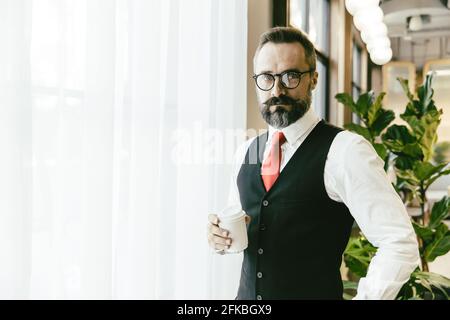 Portrait sérieux professionnel conservateur adulte modèle homme d'affaires latin barbe debout porte-tasse à café dans un bureau moderne avec espace de copie pour t Banque D'Images
