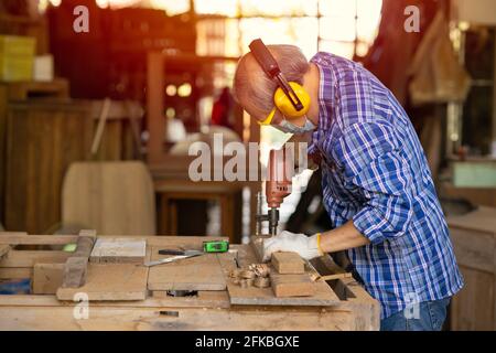 Travailleur aîné bois woodcraft retraite hobby pour la bonne retraite, asiatique homme mature maître professionnel de la fabrication de meubles en bois avec masque protecteur Banque D'Images