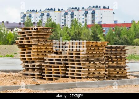 Pile de vieilles palettes en bois de stockage de matériaux en bois sur un chantier de construction sur le fond de maisons urbaines modernes. Banque D'Images