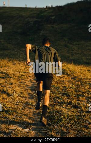 Vue arrière de l'athlète masculin qui court sur la terre pendant le coucher du soleil Banque D'Images