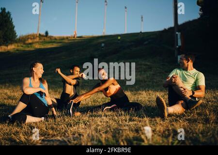 Des athlètes masculins et féminins heureux faisant de l'exercice d'étirement sur la terre au coucher du soleil Banque D'Images