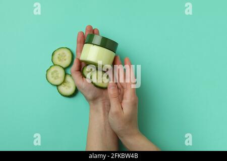 Les mains des femmes tiennent le pot avec des cosmétiques sur fond de menthe avec tranches de concombre Banque D'Images