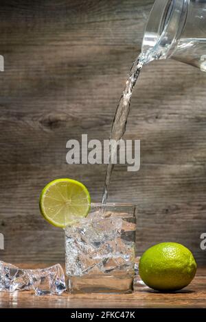 pichet d'eau versé dans un verre avec de la glace et une tranche de lime. Banque D'Images