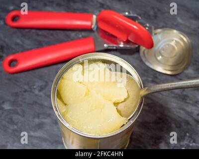 Gros plan de dessus de POV d'une grande cuillère soulevant quelques tranches de pamplemousse dans le jus d'une boîte récemment ouverte, avec l'ouvreur et le couvercle à proximité. Banque D'Images