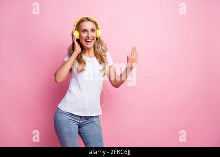 Photo de belle femme blonde optimiste danse écouter musique porter t-shirt blanc isolé sur fond rose pastel Banque D'Images