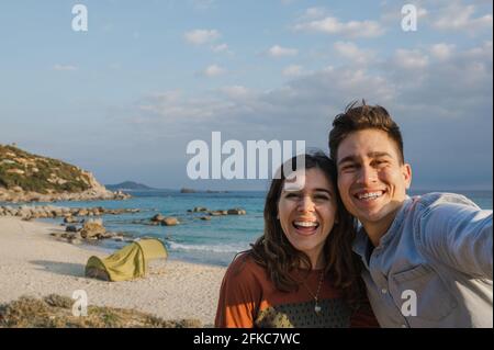 joyeux jeune couple joyeux appréciant tout en prenant une photo de selfie pendant une tente de camping sur la plage. Banque D'Images