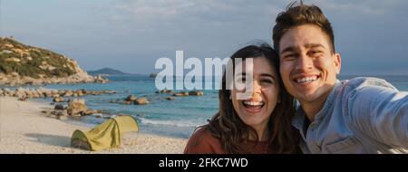 Bannière horizontale ou en-tête heureux joyeux jeune couple appréciant tout en prenant une photo de selfie pendant une tente de camping sur la plage. Banque D'Images