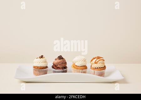 Plateau blanc de délicieuses saveurs de cupcakes sur un fond crème Banque D'Images