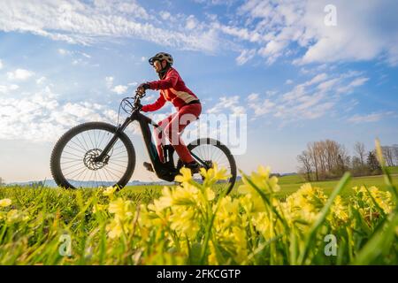 Jolie femme de milieu d'âge à monter son vélo électrique de montagne au début du printemps dans les montagnes Allgau près d'Oberstaufen, dans la lumière chaude du soir avec bloomi Banque D'Images