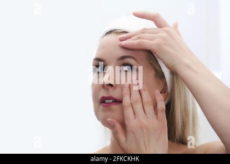 belle femme d'âge moyen fait l'auto-massage du visage autour du yeux devant un miroir Banque D'Images