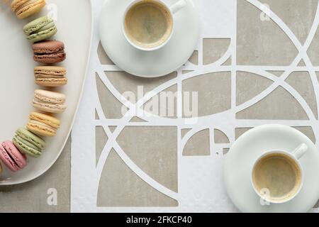 Tasses à café, macarons, cercles de séquence Fibonacci. Espresso, perfection savoureuse. Golden ratio concept, fleurs en papier, roses blanches. Vue de dessus, plan d'appartement Banque D'Images