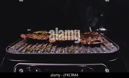 Délicieux bifteck de viande juteuse sur le gril. Faire cuire au bœuf à la sauce au roaster électrique, au romarin, au poivre noir et au sel. Ralenti. Banque D'Images