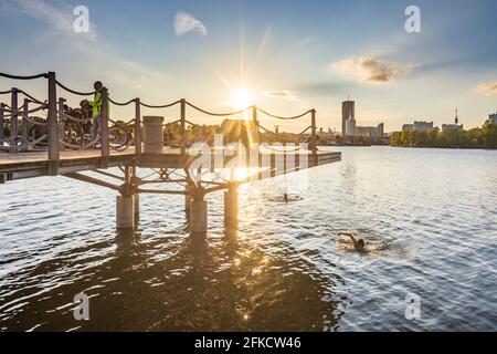 Wien, Vienne: Nageur au lac oxbow Alte Donau (Vieux Danube), jeunes assis sur une plate-forme au-dessus du lac, coucher de soleil, bâtiments de Donaucity, DC Tow Banque D'Images